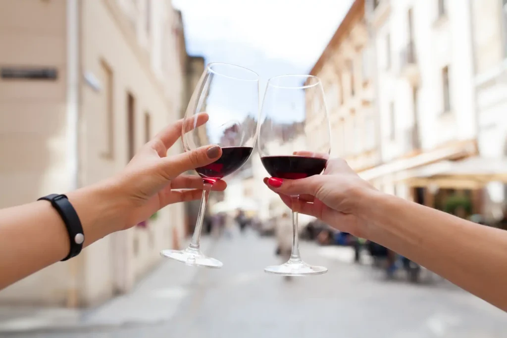 Pictured are two people toasting with two glasses of red wine.